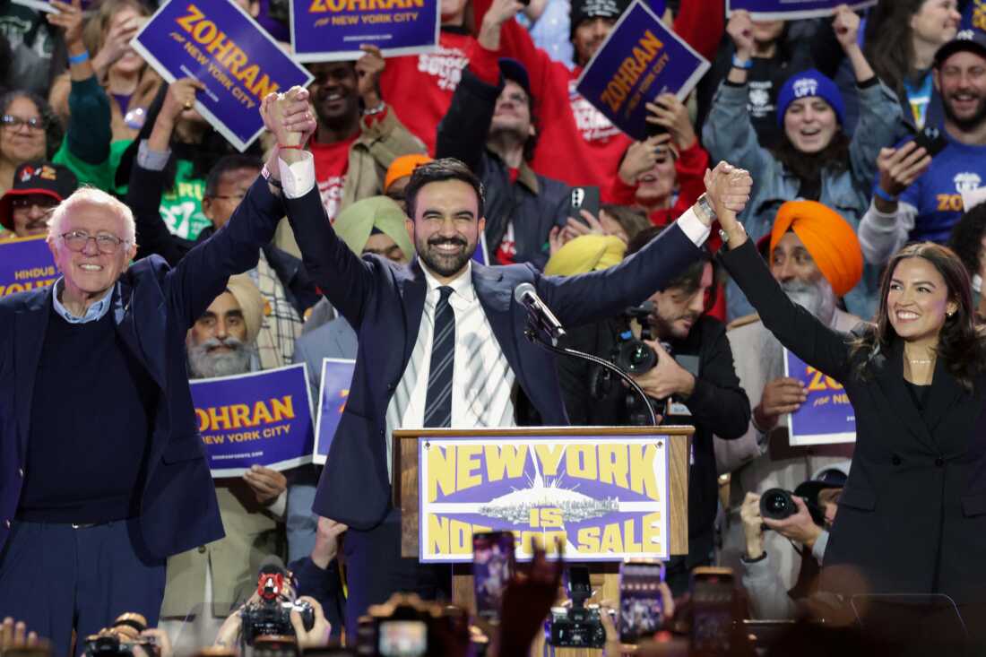 New York City mayoral candidate Zohran Mamdani (C) holds hands with US Senator Bernie Sanders (I-VT) (L) and US Representative Alexandria Ocasio-Cortez (D-NY) at the end of a campaign rally at Forest Hills Stadium in the Queens borough of New York City on October 26, 2025